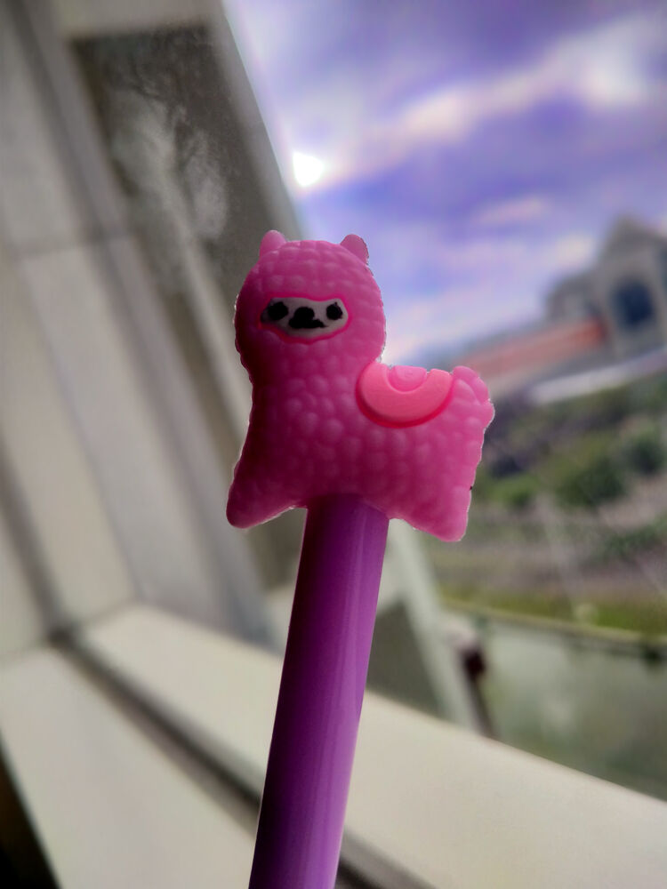 Pink alpaca-shaped pen top in front of a window and a cloudy sky