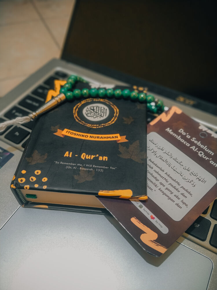 A Qur'an and green prayer beads resting on a laptop keyboard